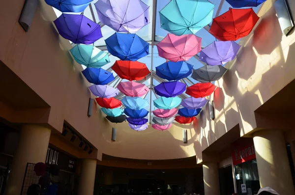 Summer multi-colored umbrellas are suspended for display at the exhibition. Many colorful umbrellas with sunlight. The ceiling in the store is decorated with rainbow umbrellas to attract customers..