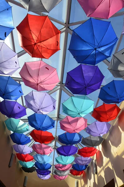 Summer multi-colored umbrellas are suspended for display at the exhibition. Many colorful umbrellas with sunlight. The ceiling in the store is decorated with rainbow umbrellas to attract customers..