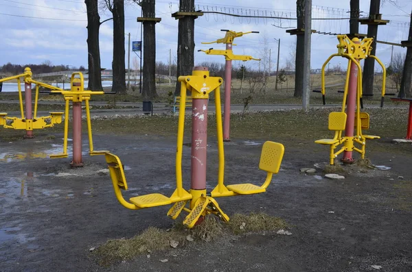 Sports simulators on the playground: horizontal bars and other equipment.One colored metal sports simulator on the street in the green grass on the lake.Sports ground.