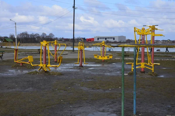 Sports simulators on the playground: horizontal bars and other equipment.One colored metal sports simulator on the street in the green grass on the lake.Sports ground.