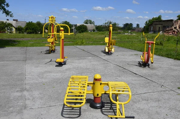 Sports simulators on the playground: horizontal bars and other equipment.One colored metal sports simulator on the street in the green grass on the lake.Sports ground.