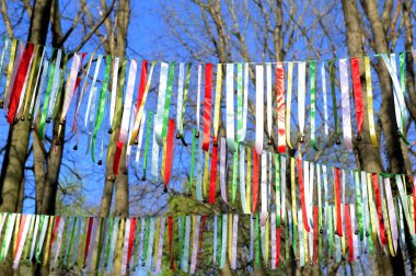 Ormanda ağaçların arasında asılı küçük çanları olan renkli kurdeleler. Geleneksel halk dekorasyonu şenlikli bir atmosfer, folklor motifleri, ilkbahar ya da yaz kutlamaları yaratıyor..
