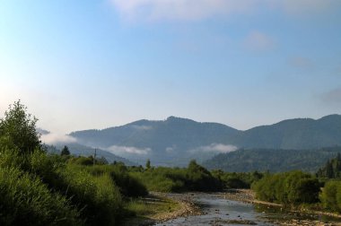 Dağların üzerinde gün doğumu. Puslu bir sabah manzarası. Dağların üzerinde sis ve şafak vakti mavi bir gökyüzünün altında orman..