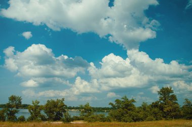 Bulutlu mavi gökyüzü, nehir ve nehir kıyısında ağaçlar.