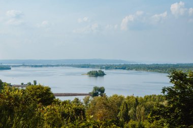 Bulutlu mavi gökyüzü, nehir ve nehir kıyısında ağaçlar.