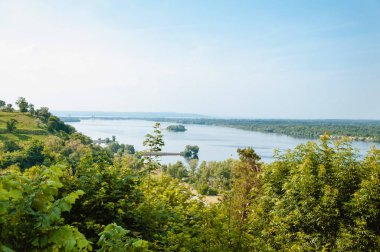 Bulutlu mavi gökyüzü, nehir ve nehir kıyısında ağaçlar.