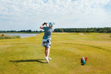 Kadın golfçü golf sahasında topa vuruyor..