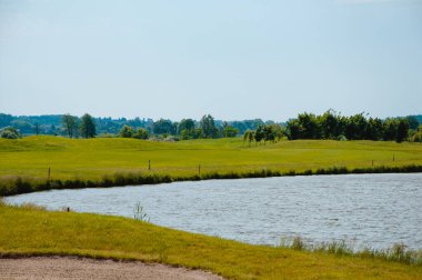 Golf sahasında göl. Güzel sülün, mavi bulutlu gökyüzü, golf sahasında ağaçlar ve çalılar.
