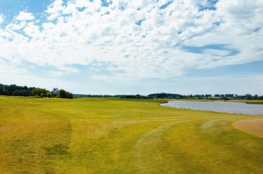 Golf sahasında göl. Güzel sülün, mavi bulutlu gökyüzü, golf sahasında ağaçlar ve çalılar.