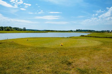 Golf sahasında göl. Güzel sülün, mavi bulutlu gökyüzü, golf sahasında ağaçlar ve çalılar.