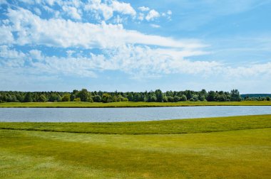 Golf sahasında göl. Güzel sülün, mavi bulutlu gökyüzü, golf sahasında ağaçlar ve çalılar.