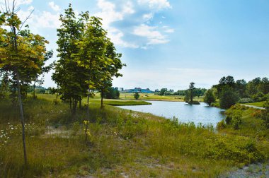 Golf sahasında göl. Güzel sülün, mavi bulutlu gökyüzü, golf sahasında ağaçlar ve çalılar.