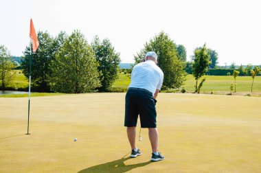 Bir sporcu golf oynar ve golf sahasında topa vurur..