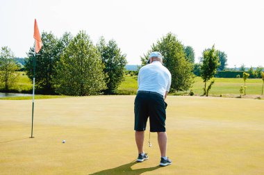 Bir sporcu golf oynar ve golf sahasında topa vurur..