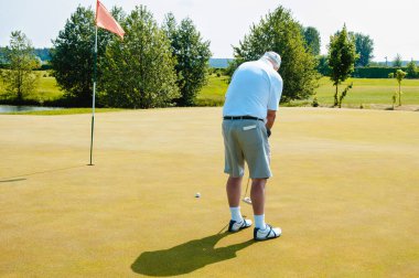 Bir sporcu golf oynar ve golf sahasında topa vurur..