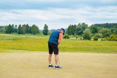 Bir sporcu golf oynar ve golf sahasında topa vurur..