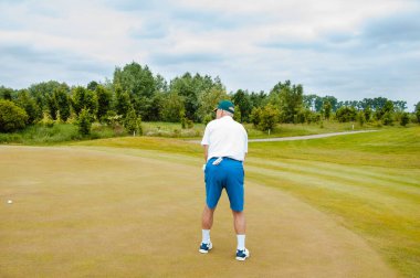 Bir sporcu golf oynar ve golf sahasında topa vurur..