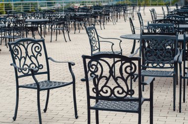 Eski moda kafe terasında dövülmüş demir masalar ve açık hava lokantası mobilyaları ile keyifli yemek alanı deneyimi.