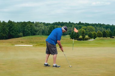 Bir sporcu golf oynar ve golf sahasında topa vurur..