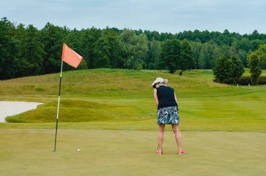 Açık havada golf sopasıyla dikilen kadın portresi. Spor giysili kadın golfçü yeşil alanda sallanıyor..