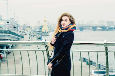 Genç güzel sarışın köprüde duruyor ve gülümsüyor. Kış portresi.