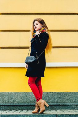 Sarı duvara karşı duran, kışlık elbiseli ve hayalleri olan genç, güzel bir sarışın. Kış portresi.