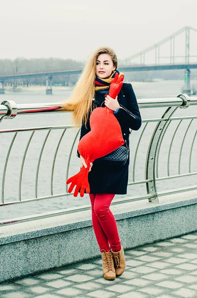冬の遊歩道で彼女の手に赤い座席おもちゃで美しい若い陽気なブロンド バレンタインデー — ストック写真