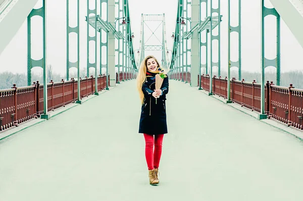 美しいです若いですブロンドとともに花束で冬には橋の上に笑顔 — ストック写真
