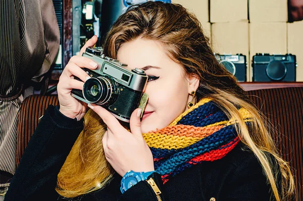 ヴィンテージカメラを持つ若い美しいブロンドの女性がカフェで写真を撮ります 写真家の冬の肖像 — ストック写真