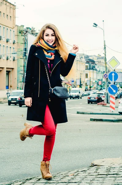 冬服の若い美しいブロンドは 街の背景と笑顔を背景に歩道に立っています — ストック写真