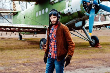 Eski bir uçağın arka planında sakallı genç bir pilot..