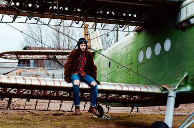 Sakallı genç pilot eski bir uçağın kanadında oturuyor..