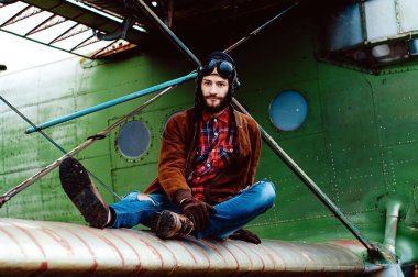 Sakallı genç pilot eski bir uçağın kanadında oturuyor..