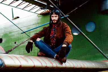 Sakallı genç pilot eski bir uçağın kanadında oturuyor..