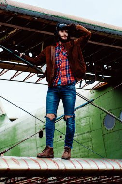 Sakallı genç pilot, eski bir uçağın kanadında dikiliyor..