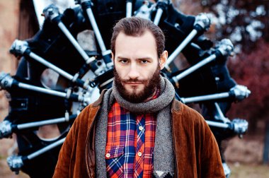 Sakallı bir adam, bir pilot, bir gezgin eski bir uçağın turbo pervane motorunun arka planında duruyor..