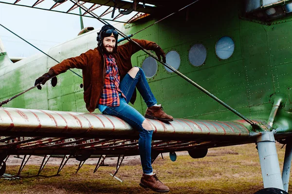 Sakallı genç pilot eski bir uçağın kanadında oturuyor..