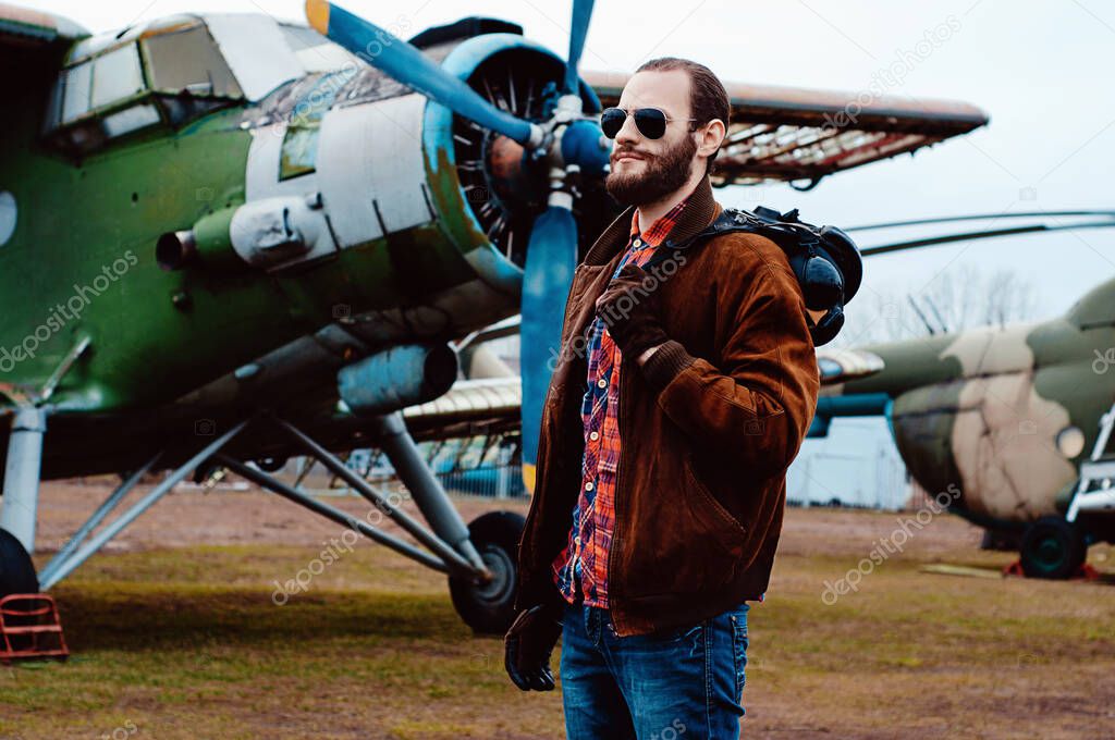 Bearded young pilot on the background of a vintage aircraft.