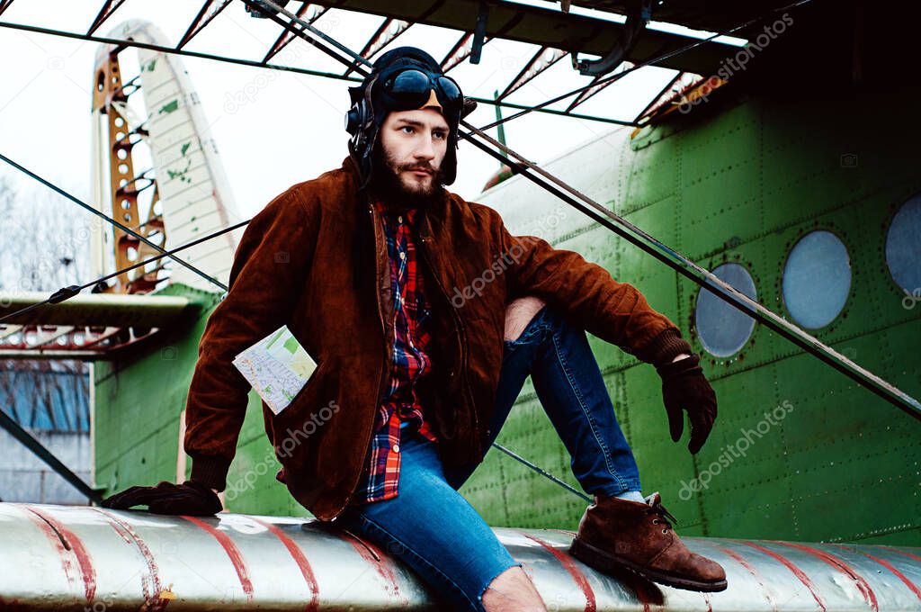 bearded young pilot sits on the wing of an old plane.