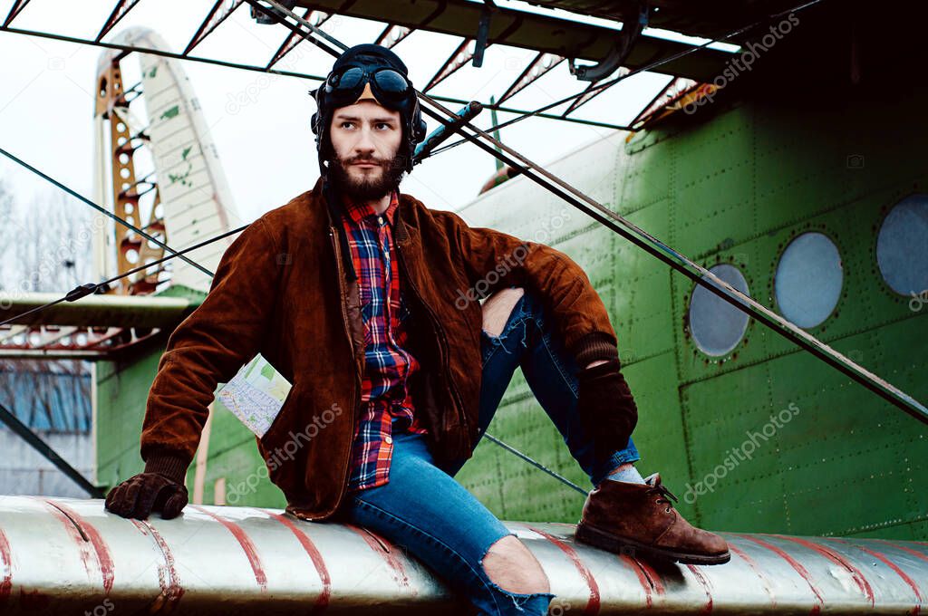 bearded young pilot sits on the wing of an old plane.