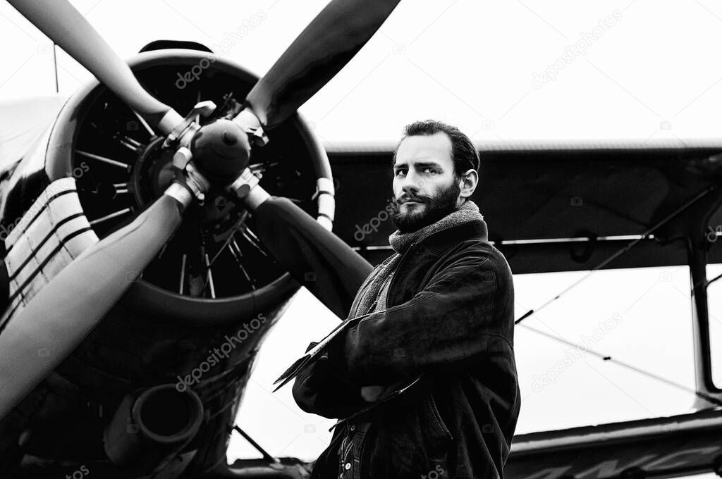 A bearded young pilot, a traveler stands on the background of a red vintage aircraft. Black and white photo.