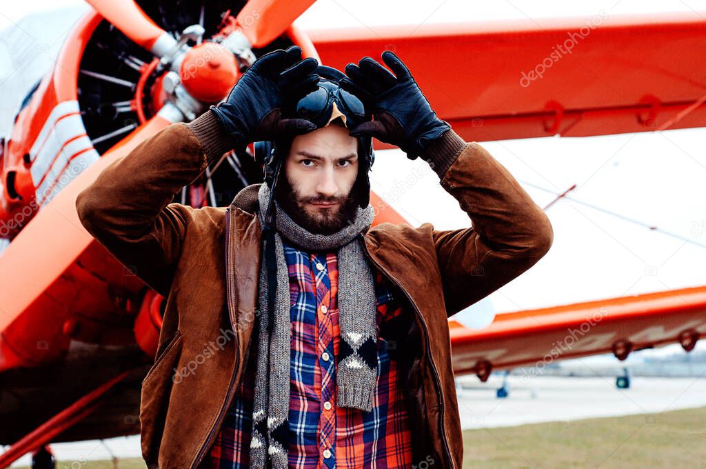 A bearded young pilot, a traveler stands on the background of a red vintage aircraft.