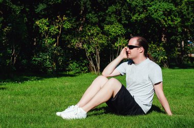 Parkta çimlerin üzerinde oturan bir adam telefonda konuşuyor.