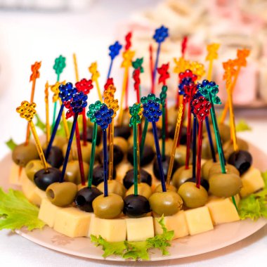 Sert peynir ve zeytin aperatifleri, çok renkli kılıçlarda, beyaz bir tabakta, marul yapraklı..