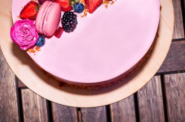 Bisküvi, reçel, ahududu, çilek, yabanmersini ve ahududu gülleriyle süslenmiş şenlikli pembe bir pasta..
