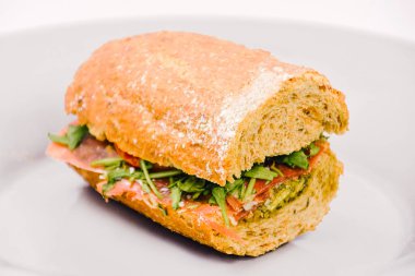 Beyaz arka planda beyaz bir tabakta hardallı sosisli sandviç.