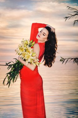 Temmuz 2015 'te Kiev Denizi' nin kıyısında uzun kırmızı elbiseli, bir buket zambak taşıyan güzel hamile esmer.