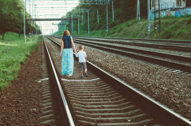 Anne ve oğul, trenin geçtiği raylarda yürüyor.