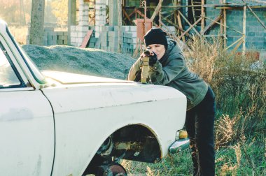 Terk edilmiş bir eve dayanmış bir kız, bozuk bir arabaya ateş ediyor.