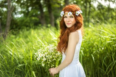 Uzun kızıl saçlı bahar güzeli kız dışarıda saç üflüyor. Çiçek açan ağaçlar. Romantik genç kadın portresi. Doğa